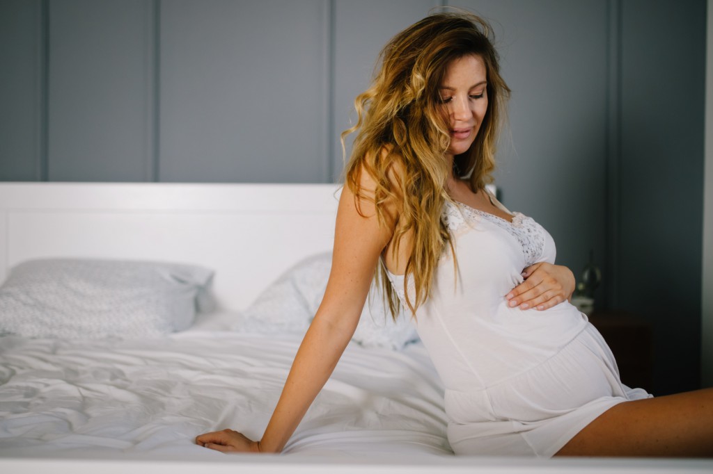 Portrait of attractive young pregnant woman sitting on bed